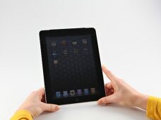 Frau in gelbem Oberteil hält Apple iPad in beiden Händen.