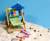 Liegestuhl mit Sonnenschirm und Flip Flops im Sand