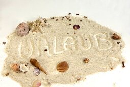 "Urlaub" im Sand geschrieben mit Muscheln drum herum