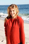 blonde Frau in orangefarbenem Pulli am Strand