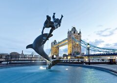 Sculpture of dolphin with girl and Tower Bridge in background at Southwark, London, UK