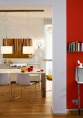 A view into a dining room with a table, chairs and a modern pendant lamp