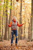 Happy blonde woman wearing gray puffer jacket throwing autumn leaves in air