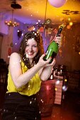 Portrait of happy woman wearing yellow top celebrating New Year's with champagne, smiling