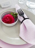 Place setting with fork as napkin ring and rose in bowl