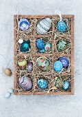Blue, hand-painted Easter eggs in a wooden seedling tray lined with straw