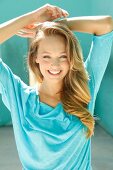 Portrait of beautiful blonde woman wearing turquoise top smiling with hand behind head