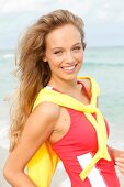 Portrait of pretty woman wearing red sporty top and yellow coat over shoulder, smiling