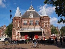 Tourists standing and cycling outside Waag monument in Nieuwmarkt, Amsterdam, Netherlands