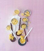 Various types of pasta on ladles on a pink-checked cloth