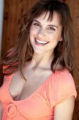 Portrait of attractive woman with brown hair in orange top standing against wooden wall