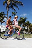Paar hat Spaß auf einem Rad sie sitzt auf Lenker, Palmen