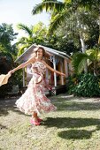 Happy woman in floral pattern dress dancing in front of log cabin, smiling