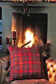 Red cushion in plaid fleece cover on leather chair in front of fireplace