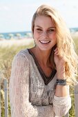 Portrait of pretty blonde woman wearing jumper with v neck standing on beach, smiling