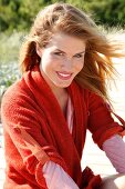 Portrait of beautiful blonde woman with windswept hair wearing red sweater, smiling