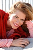 Portrait of attractive woman wearing red sweater and pink top lying on sand, smiling