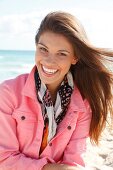 Dark-haired woman in a pink denim jacket, laughing by the sea