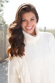 Dark-haired woman in a white turtleneck, laughing by the sea