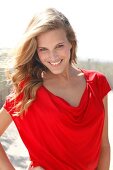 Portrait of attractive woman wearing red top standing on beach, smiling