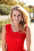 Blonde woman in a red dress on the beach, smiling and looking at camera