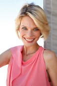 Portrait of happy blue eyed blonde woman with short hair wearing pink top, smiling