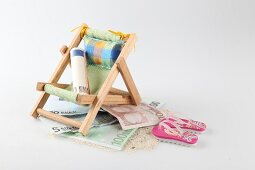 Rolled-up currency on small deck chair with flip-flops and sand
