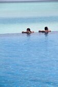 Man and woman relaxing in pool with sea in background in Dhigufinolhu Island, Maldives