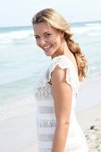 blonde Frau im weißen Kleid am Strand, lacht in die Kamera