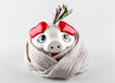 Close-up of piggy bank wrapped with beige scarf against white background