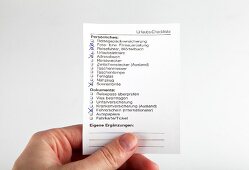 Close-up of hand holding travel checklist for vacation against white background