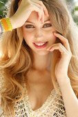 Portrait of beautiful blonde woman with long hair wearing bracelet and netted top, smiling