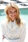 Portrait of blonde woman wearing white turtleneck sweater standing on beach, smiling