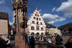People sitting around fish fountain in the Cathedral square in Freiburg, Germany