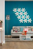 Wohnbereich mit Sofa, Stehlampe & moderner Wandleuchte vor blauer Wand