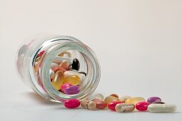 Different pills, tablets, dragees and capsules spilling out from glass bottle