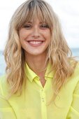 Portrait of cheerful blonde woman wearing yellow shirt sitting on beach, smiling