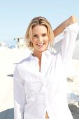 Blonde, sporty woman with long hair in a white blouse on the beach