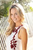 Blonde woman with long hair in a summer dress on the beach in front of a fence