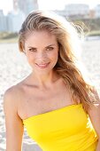 Blonde Frau mit langen Haaren im gelben Kleid am Strand