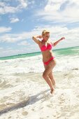Blonde Frau mit kurzen Haaren im pinkfarbenem Bikini am Strand