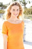 Blonde Frau mit langen Haaren in orangefarbenem T-Shirt am Strand