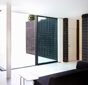 Black sofa in front of an open patio door and view of a black tiled wall in front of a white floor