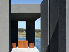 Minimalist terrace in South American country house near water with cubic wooden furniture and dark-grey wall elements