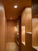Narrow hallway with wood paneling on the wall and ceiling and built-in shelves made of wood