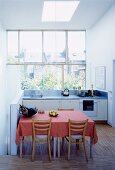 Pink tablecloth on a dining table with rustic chairs in an open, white kitchen