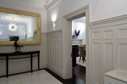 Vorraum mit weisser Holzverkleidung an Wand und offener Wohnraumtür gegenüber antiker Konsolentisch mit Spiegel