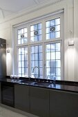 Designer kitchen counter with brown cabinets and glossy countertop in front of leaded glass windows