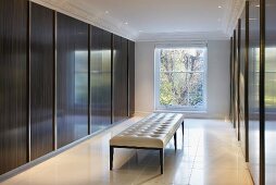 Classic bench upholstered in white leather in front of glossy, wood sliding doors in an elegant dressing room