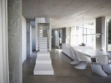 White stair landing in front of stairs in an open living room with shell chairs (in Bauhaus style) in front of a dining table